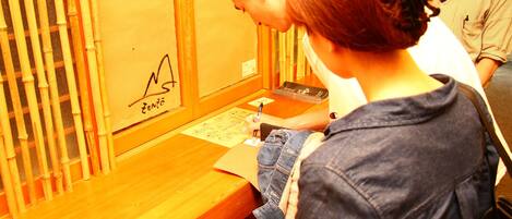 A wooden counter with a logo, a person writing on a piece of paper, and another person standing nearby.