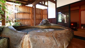 Un jardín japonés tradicional con un manantial termal de piedra, vallas de madera y vistas a un edificio tradicional.