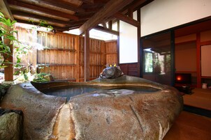 Un jardín japonés tradicional con un manantial termal de piedra, vallas de madera y vistas a un edificio tradicional.