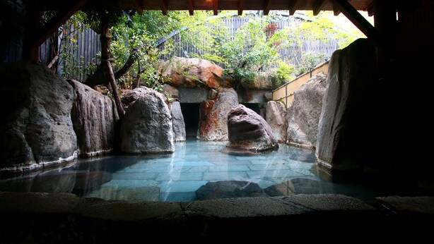 Una piscina de piedra con rocas grandes, rodeada por una estructura de madera y una valla de madera.