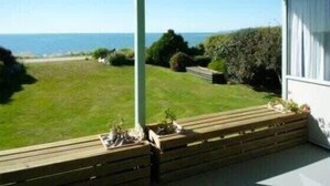 A balcony with a view of the sea, a grassy lawn, and a wooden bench. - Sunrise at Parapara Beach (Parapara)