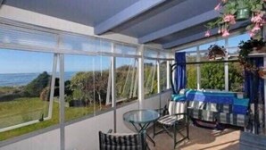 A balcony with a glass table and chairs, overlooking a coastal view. - Sunrise at Parapara Beach (Parapara)