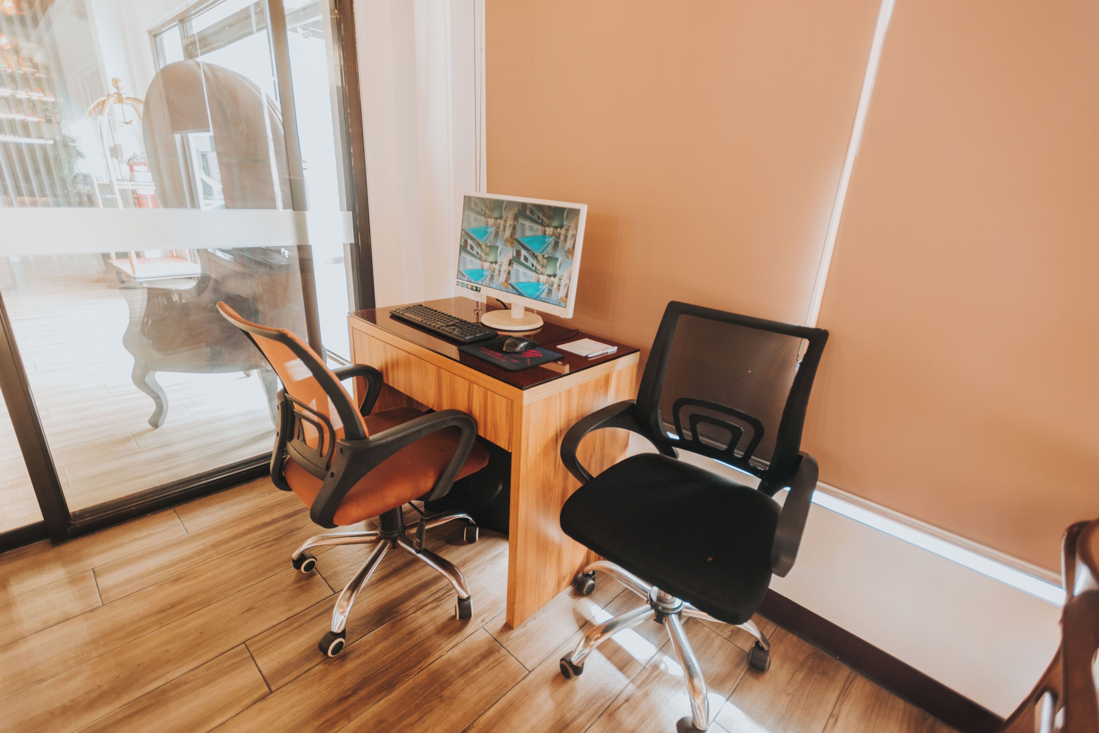 A workspace with a wooden desk, two office chairs, a computer monitor, keyboard, and mouse.