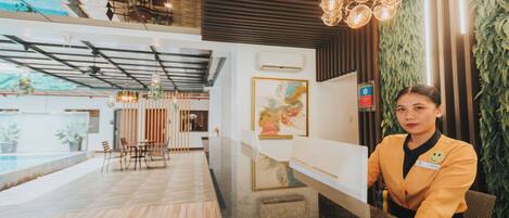 A reception area with a wooden floor, a reception desk, and a modern interior design including a hanging light fixture and a large painting on the wall.