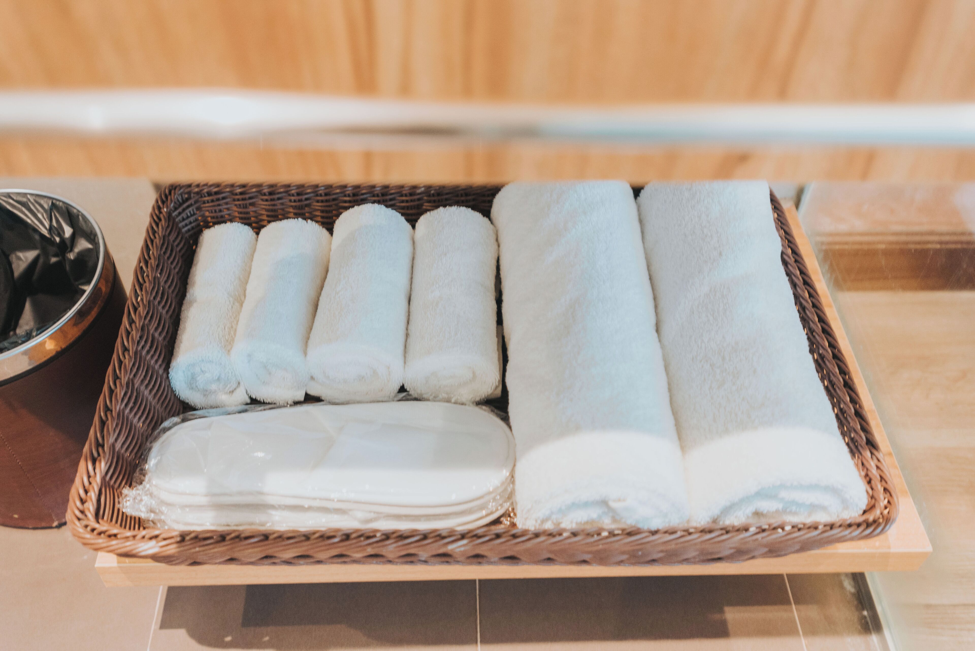A wicker basket containing neatly folded white towels and a stack of white bathmats.
