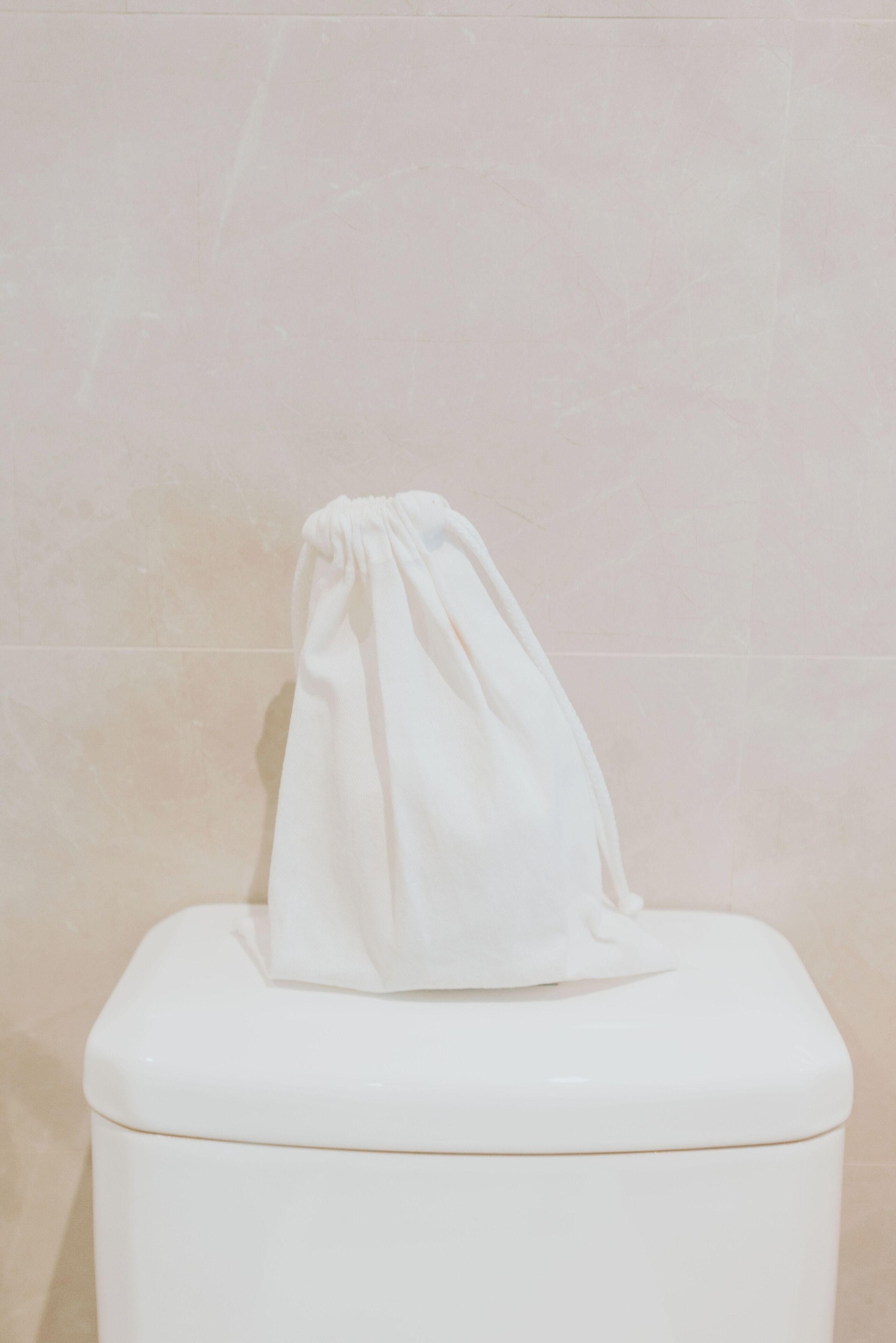 A toilet with a white bag hanging on the lid in a bathroom with beige tiles.