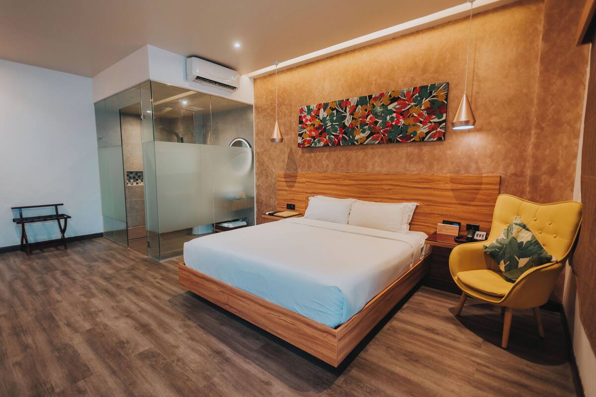 A modern bedroom with a wooden bed, a glass shower enclosure, and a yellow armchair.