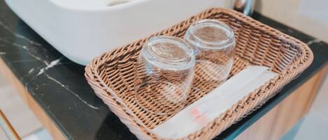 Una cesta de mimbre con dos vasos transparentes y una servilleta sobre una encimera negra.