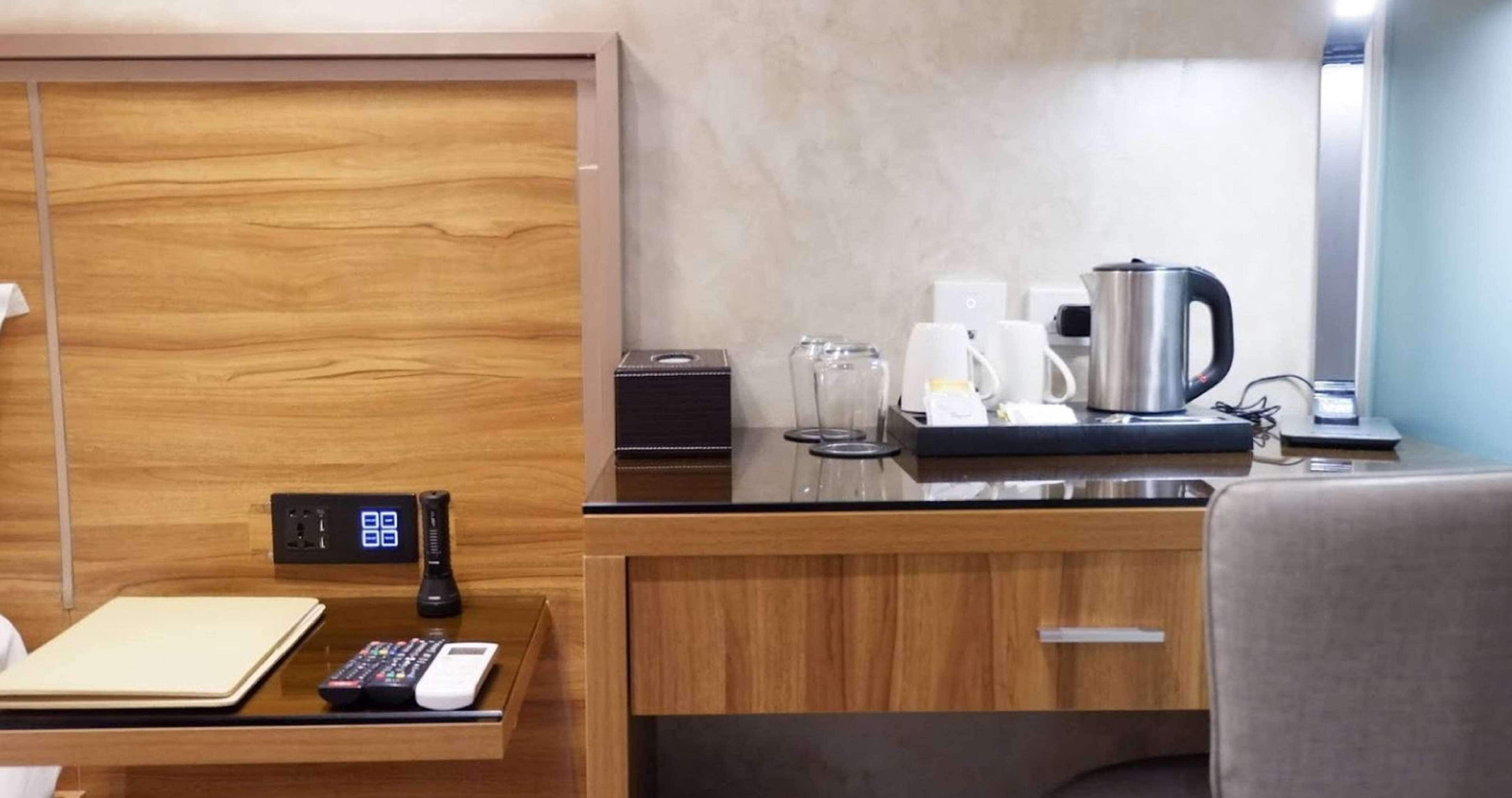 A modern hotel room with a wooden desk, a digital clock, a coffee maker, and a kettle.