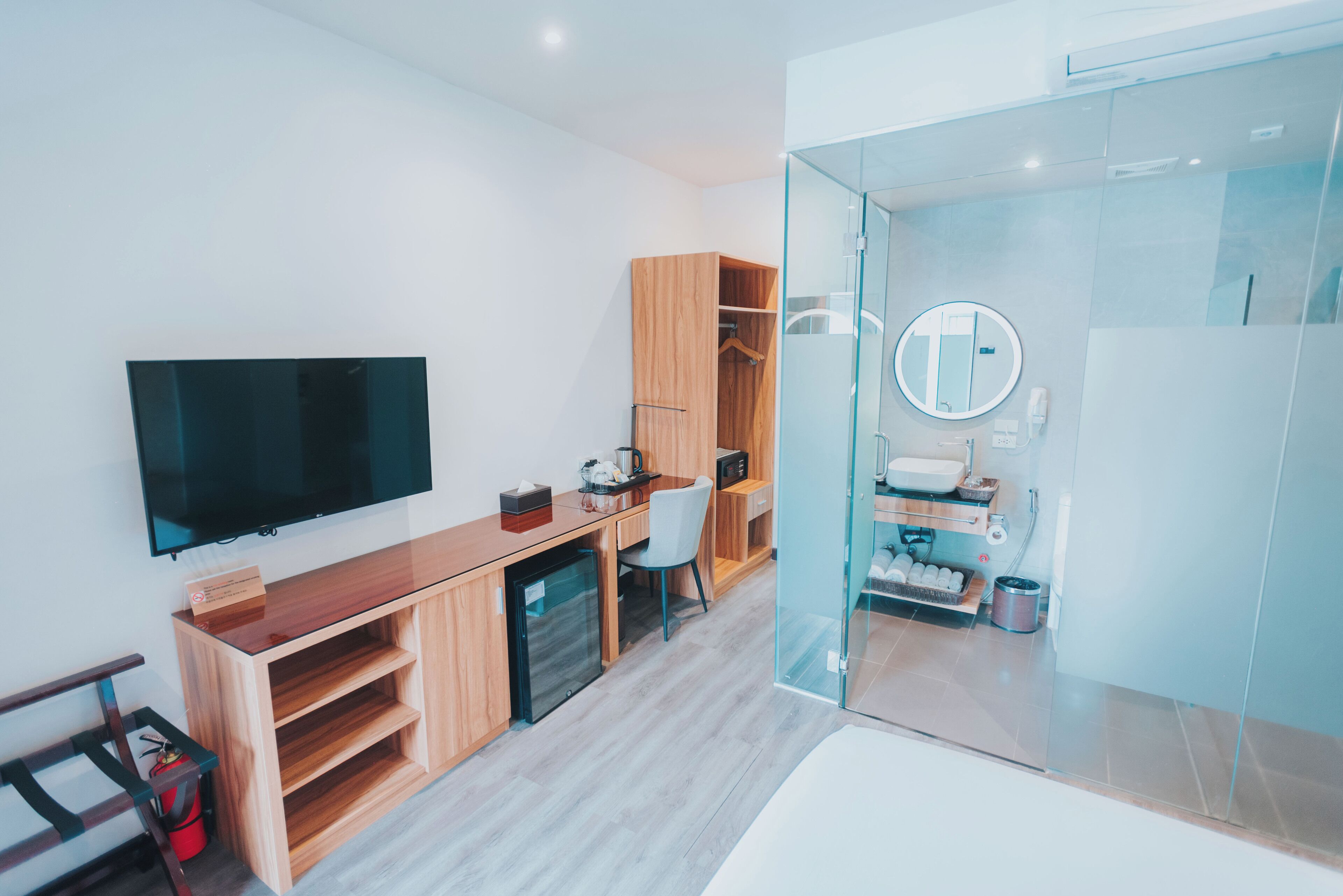A modern hotel room with a wooden desk, a flat-screen TV, a glass shower enclosure, and a built-in wardrobe.