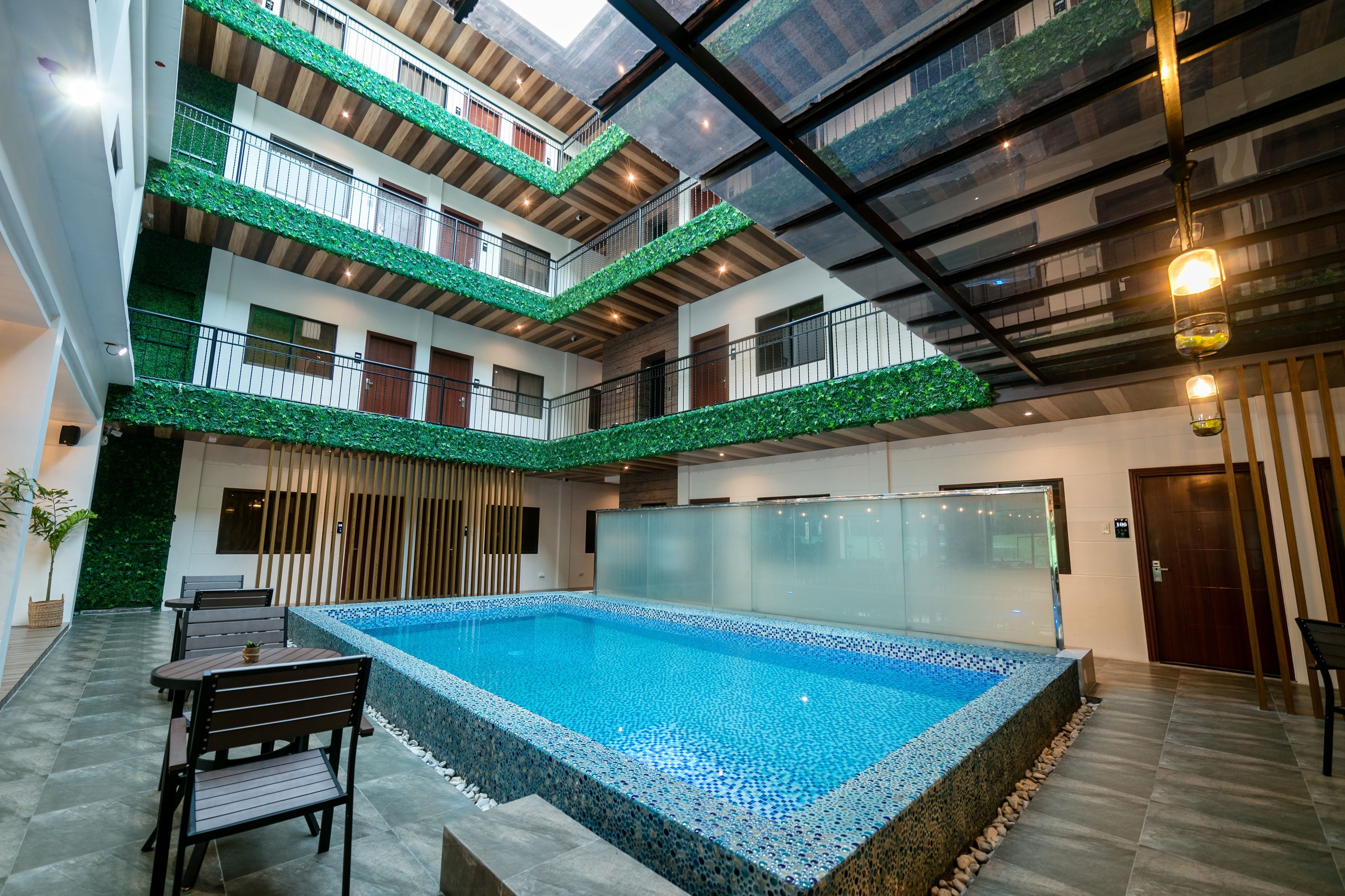 A multi-level indoor swimming pool with a glass wall, wooden flooring, and a seating area with tables and chairs.