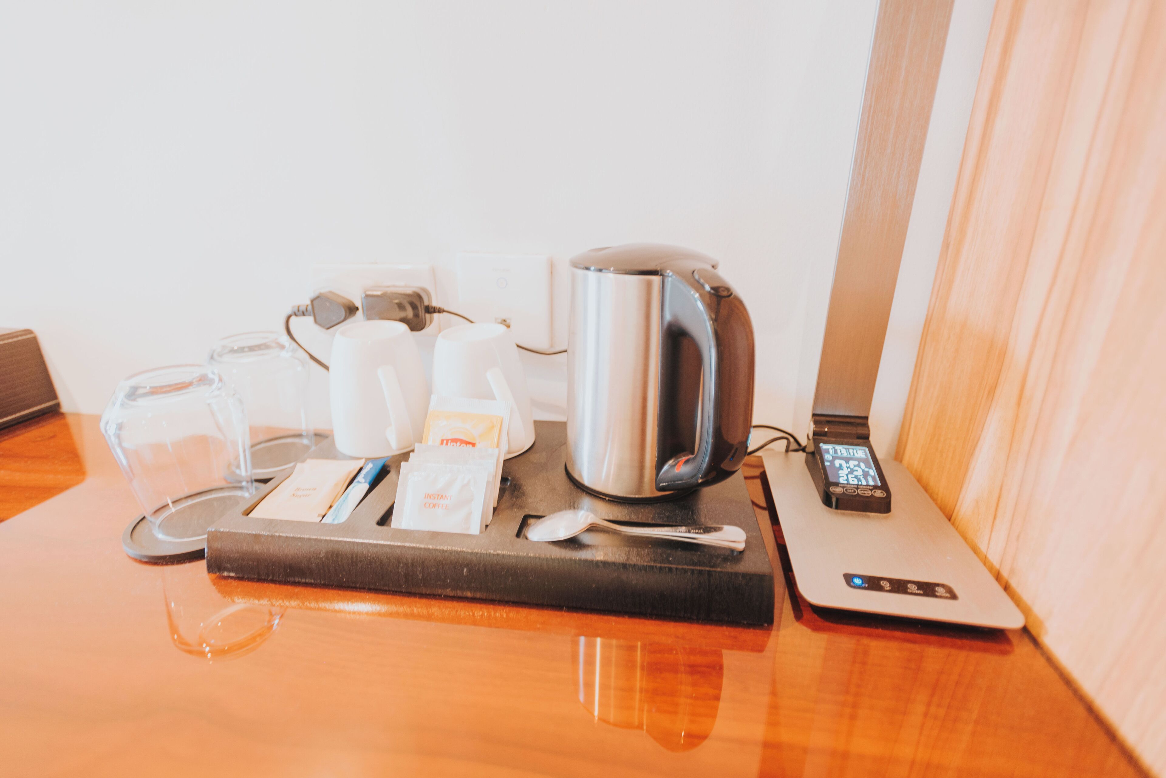 A hotel room with a coffee station including a kettle, cups, and a digital scale.