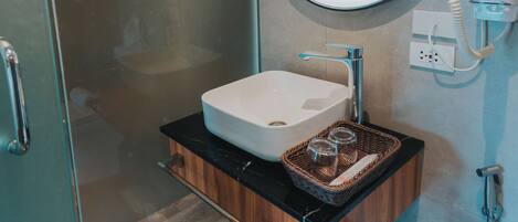 Une salle de bain moderne avec une douche à parois de verre, un miroir rond, un lavabo blanc et un meuble-lavabo en bois.