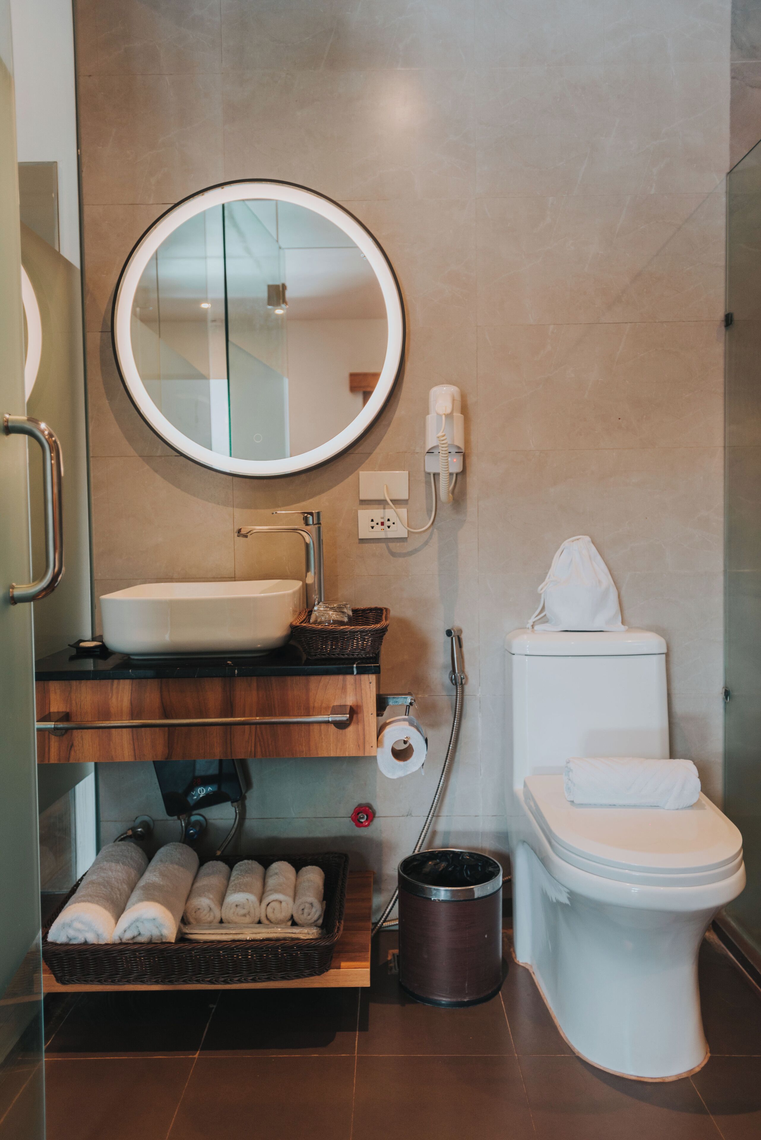 Ein Badezimmer mit rundem Spiegel, Waschbecken, Toilette und Mülleimer.