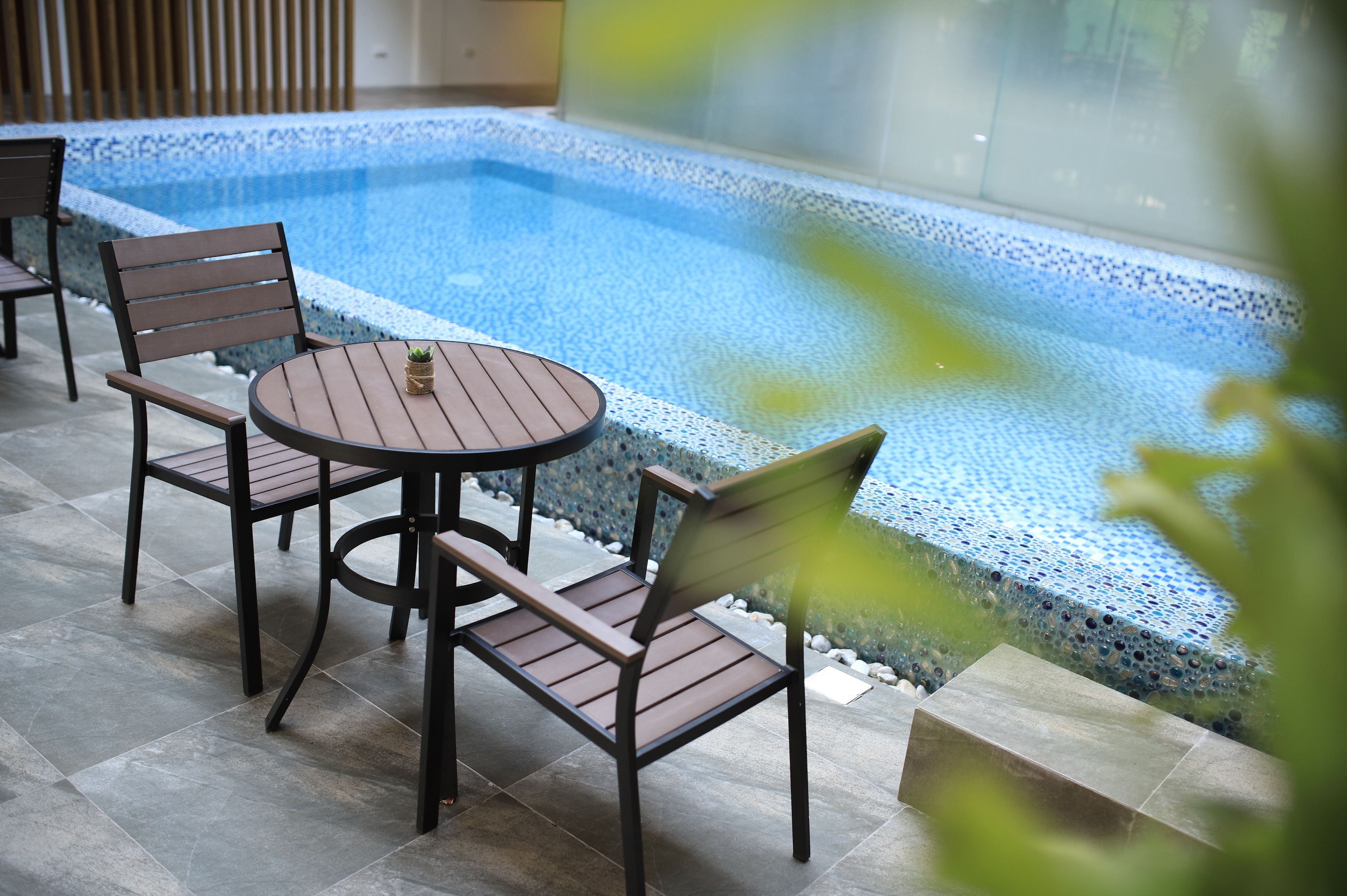 Un espace aménagé au bord de la piscine, avec une table et des chaises, une petite plante posée sur la table et une vue dégagée sur la piscine.