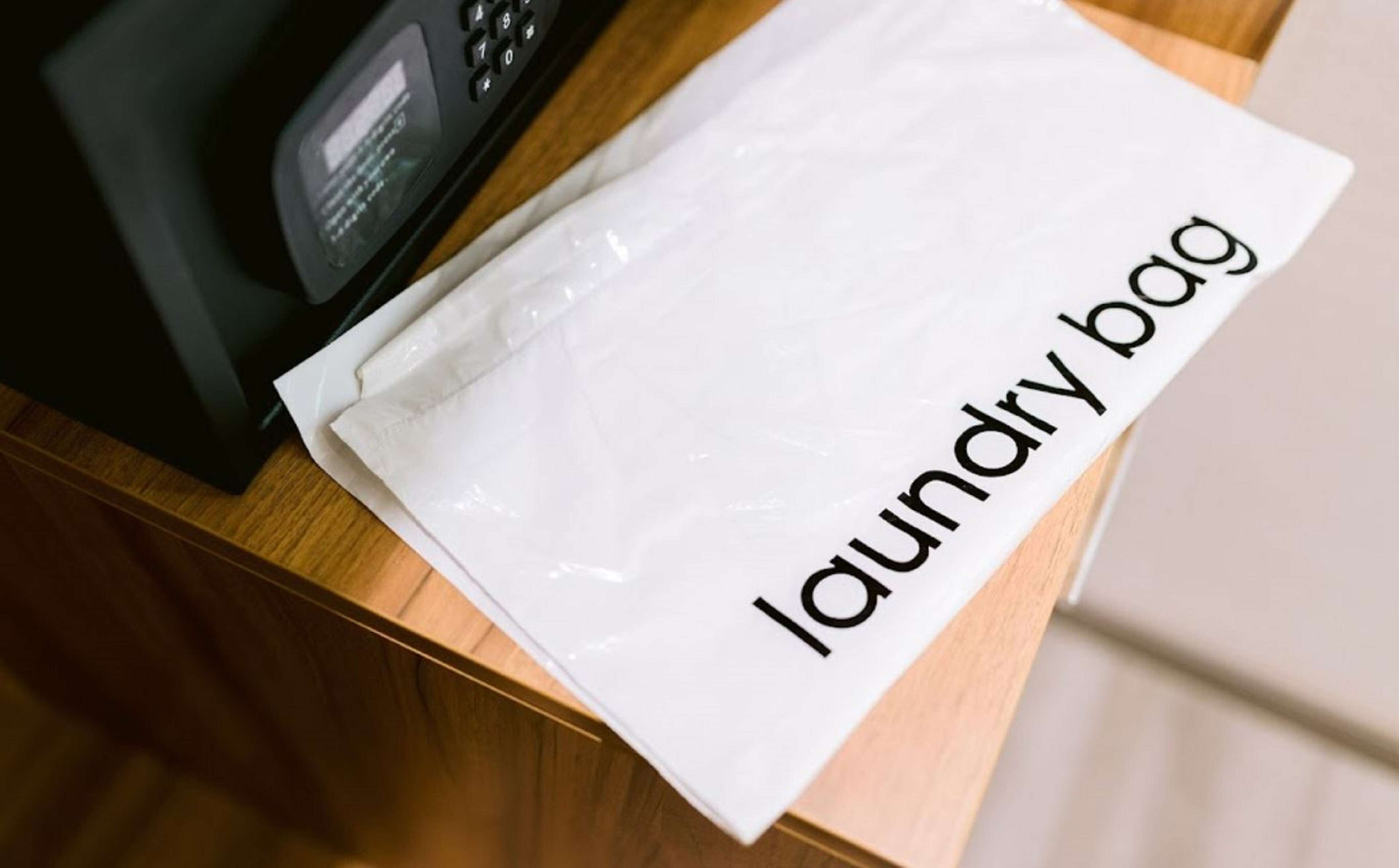 Un sac en plastique blanc, portant l’étiquette « sac à linge », est posé sur une surface en bois, à côté d’un appareil électronique noir.