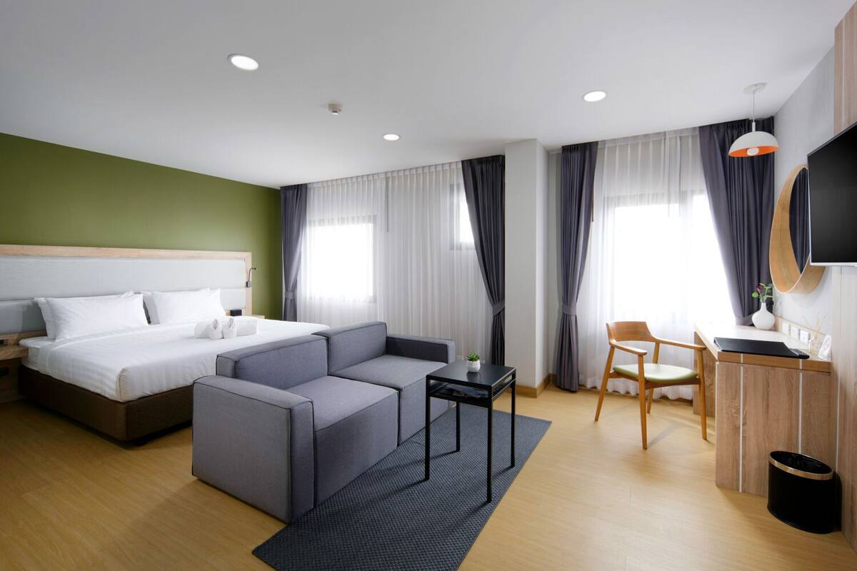 A modern hotel room with a bed, a sofa, a desk, and a TV.