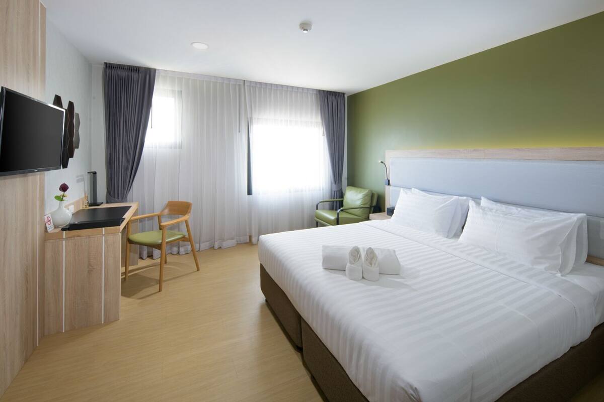 A hotel room with a large bed, a desk with a chair, a television, and a green wall.