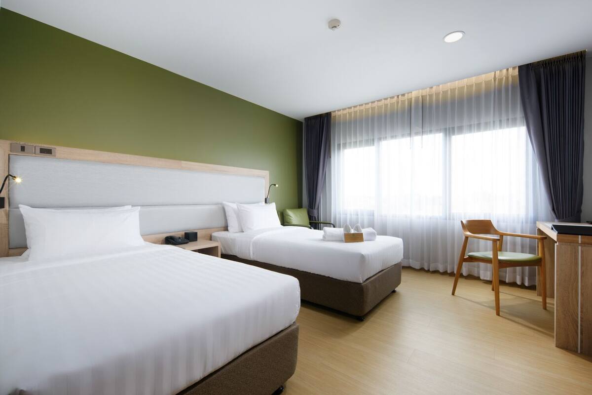 A hotel room with two beds, a desk, a chair, and a large window with curtains.