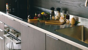 Una cocina moderna con armarios de madera oscura, electrodomésticos de acero inoxidable y una variedad de frutas y verduras frescas, además de utensilios de cocina sobre la encimera.