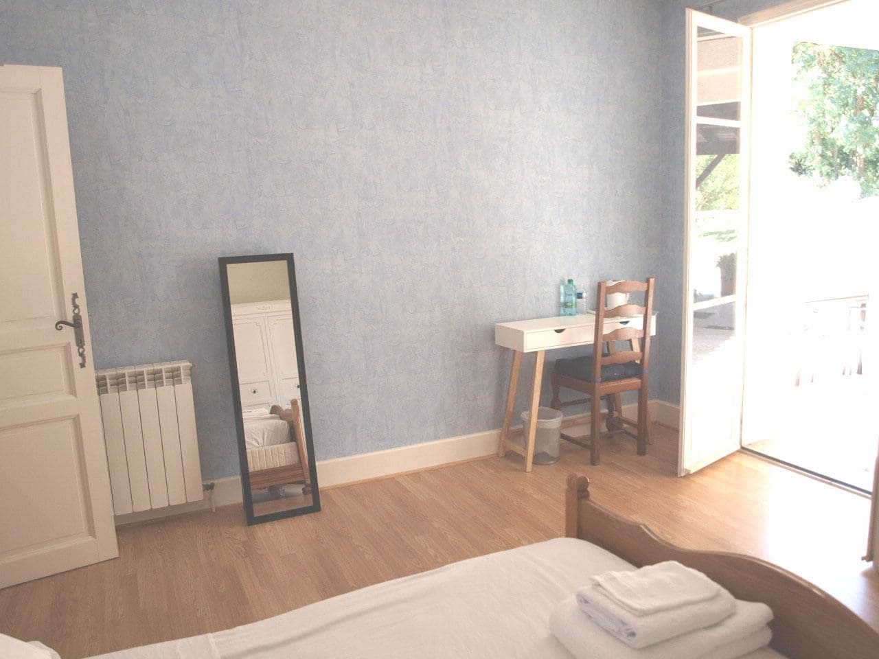A bedroom with a bed, a chair, a desk, a mirror, and a radiator.