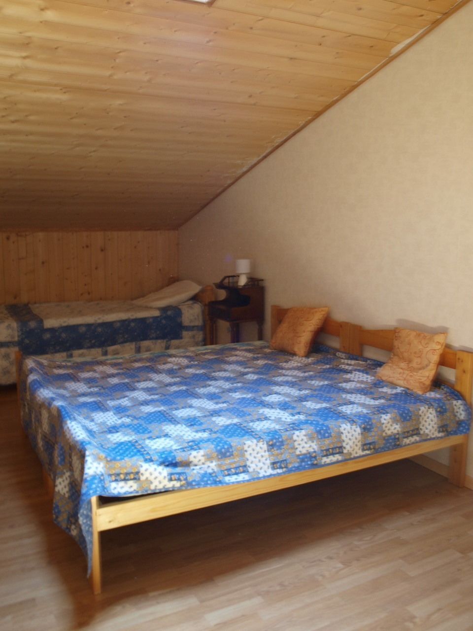 A bedroom with a wooden ceiling, a bed with a blue quilt, and a nightstand with a lamp.
