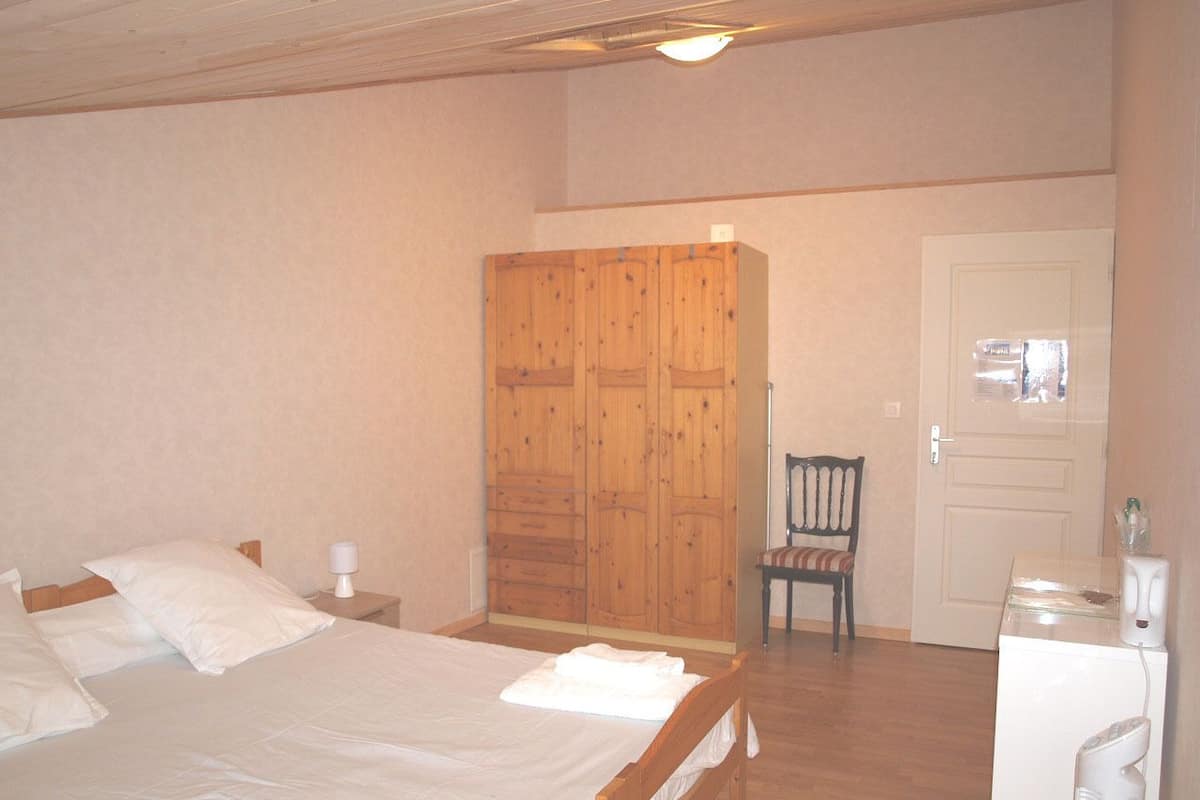 A bedroom with a wooden bed, a wardrobe, a chair, and a small white appliance.