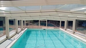 Une grande piscine intérieure à l’eau claire, entourée de murs en verre et surmontée d’un toit.