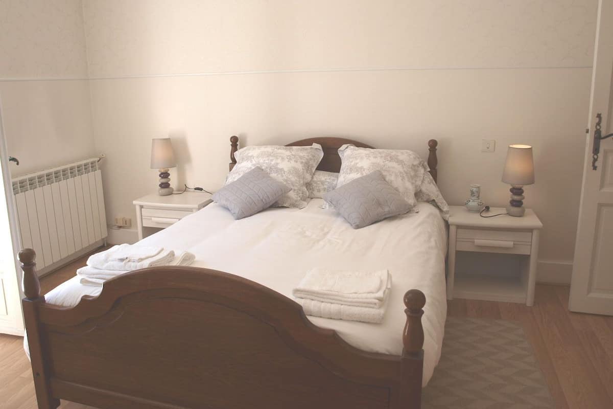 A neatly made bed with white linens and two pillows, flanked by bedside tables with lamps.