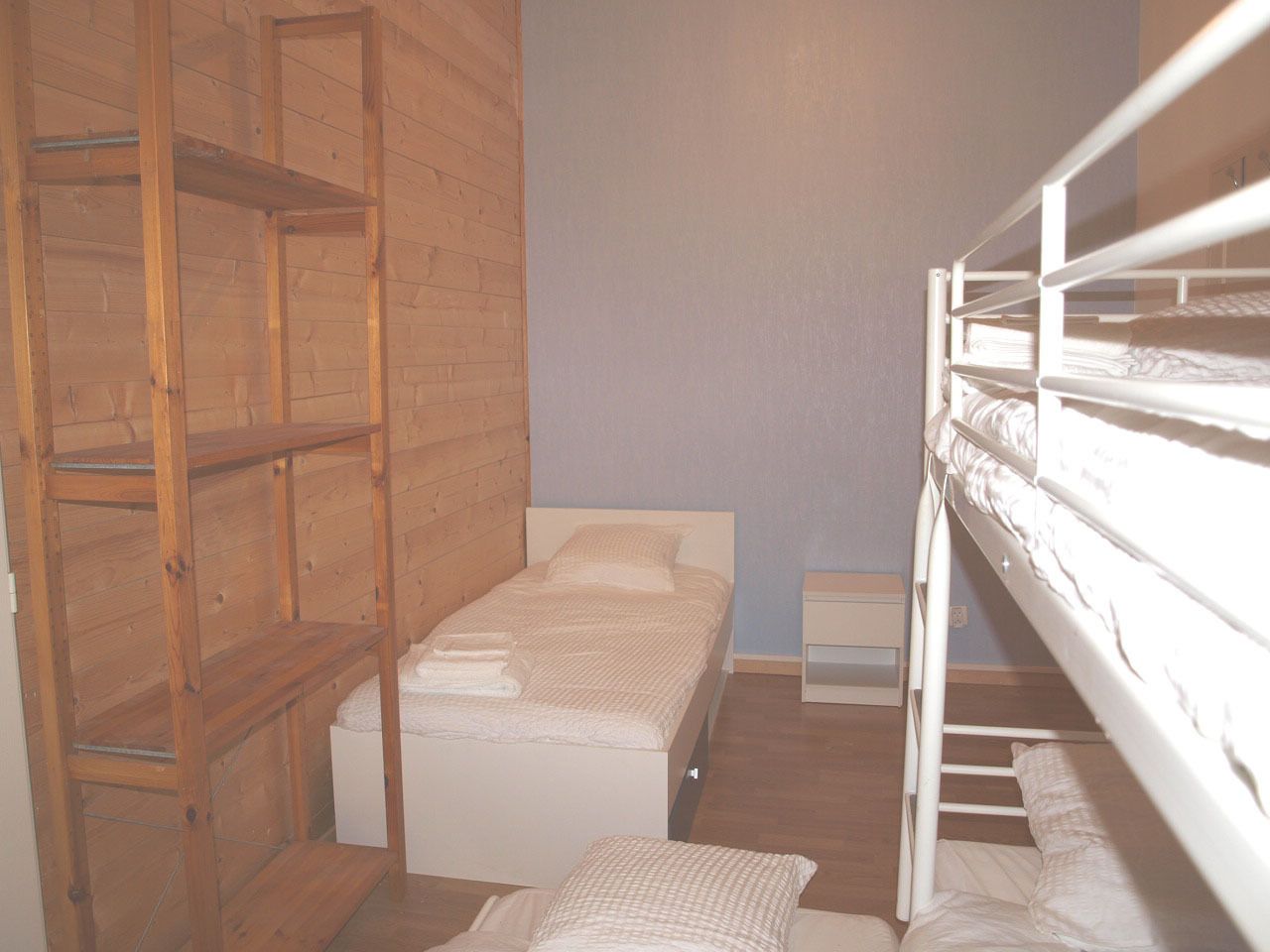 Une petite pièce, de taille modeste, comprenant un lit superposé, un lit simple et une étagère en bois.