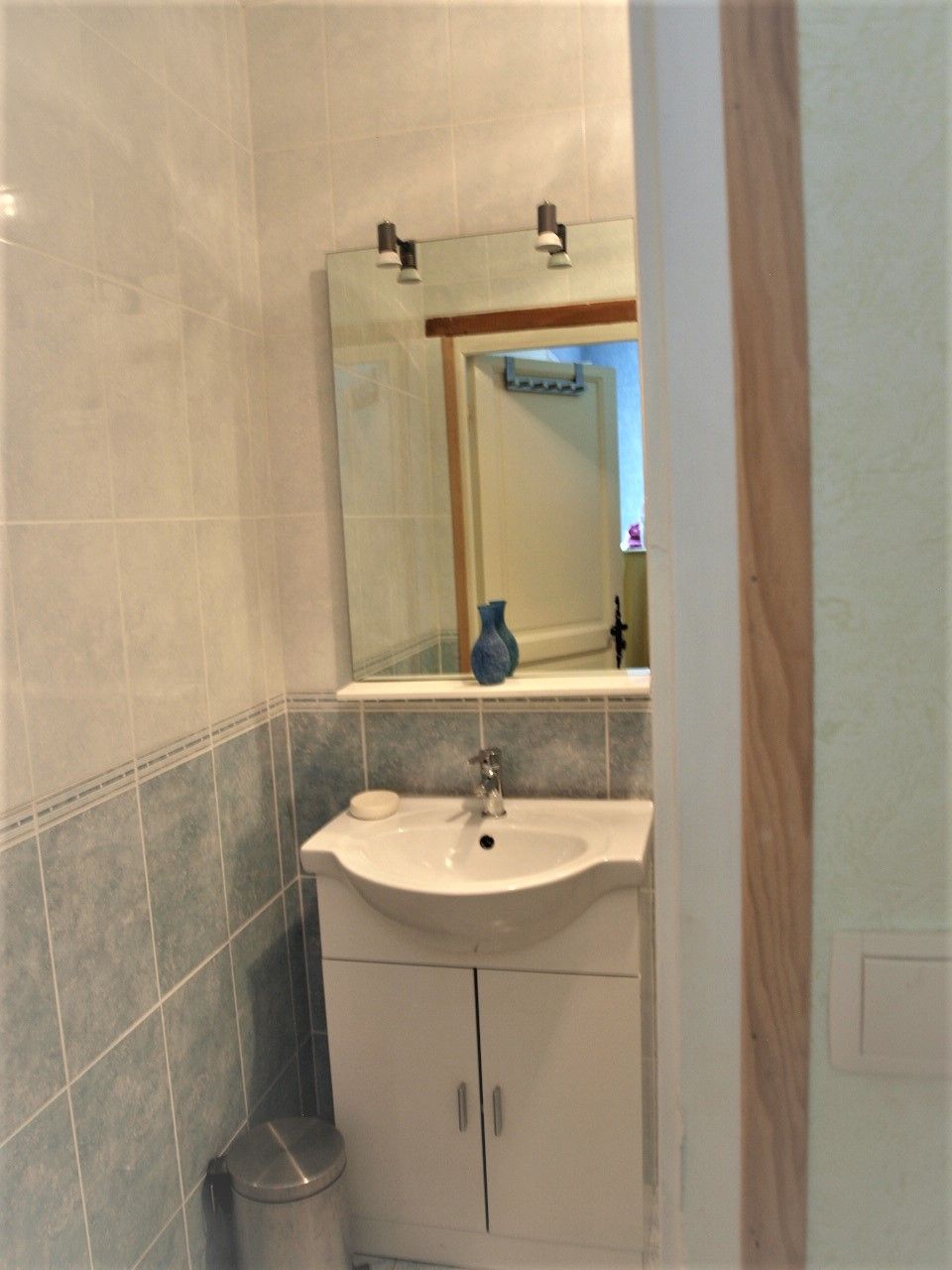 Un baño con un lavamanos blanco, un espejo y un florero azul sobre el mostrador.