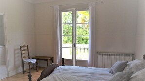 Une chambre avec un grand lit, une chaise, une petite table et une fenêtre avec des rideaux.