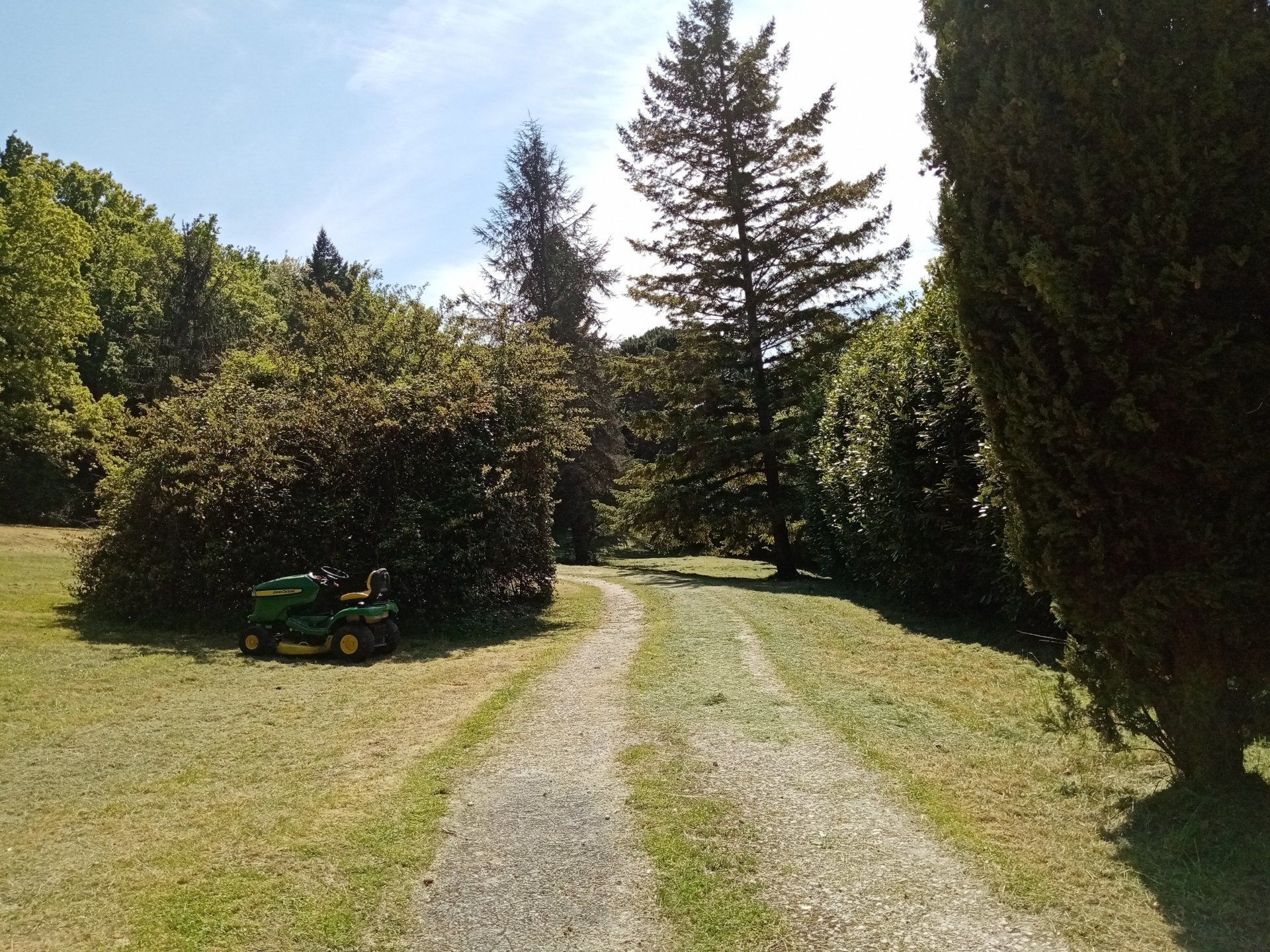 Een grindpad dat door een bebost gebied loopt, met een groene tractor aan de linkerkant geparkeerd.