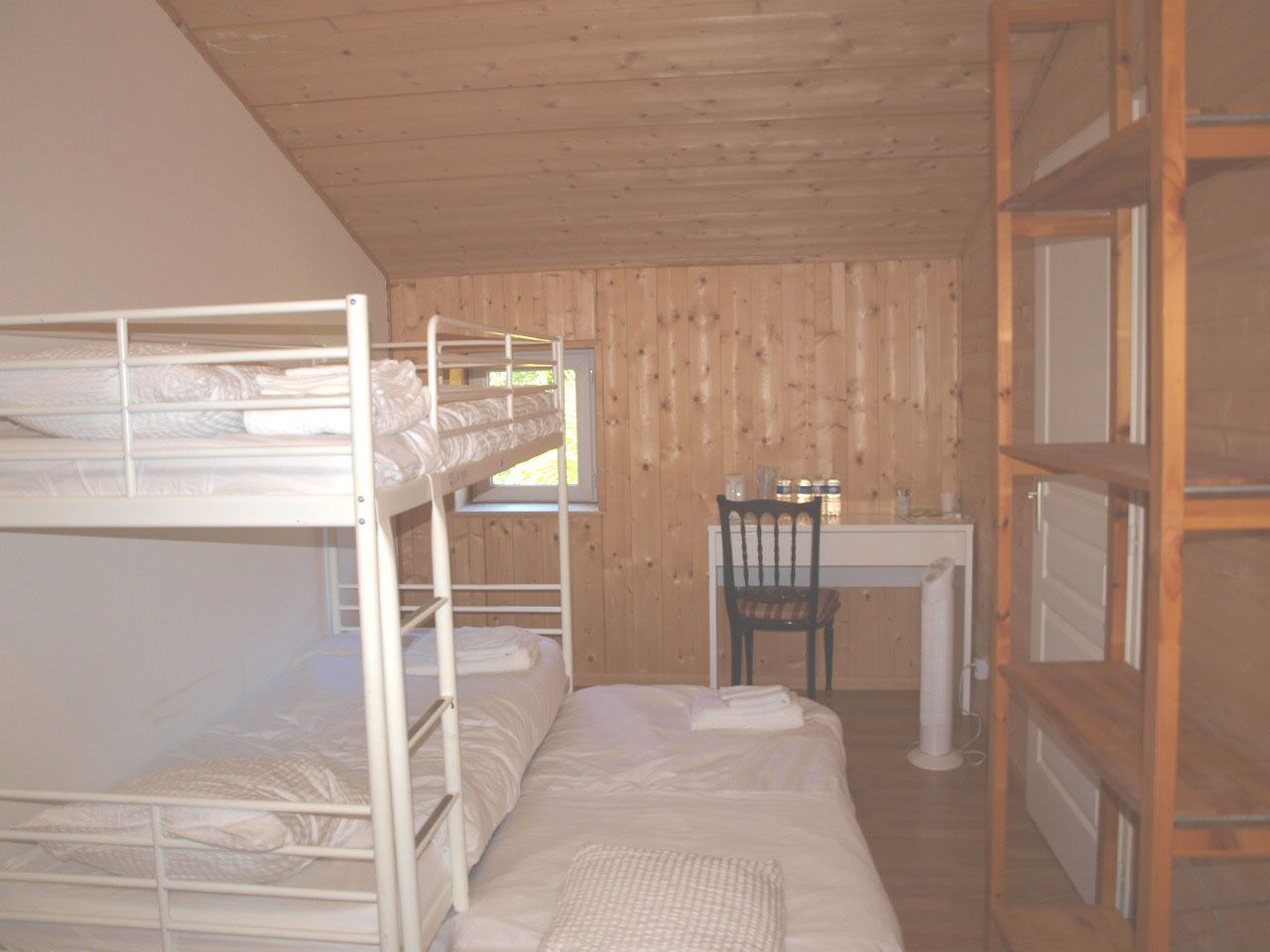 Een slaapkamer met stapelbed, bureau en stoel, houten wanden en een raam.