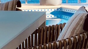 Zona de piscina con vista al mar, una mesa y sillas.