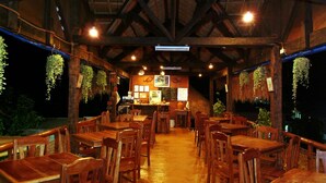 Ein Restaurant mit Holztischen und -stühlen, hängenden Pflanzen und einer Theke mit Speisekarte.