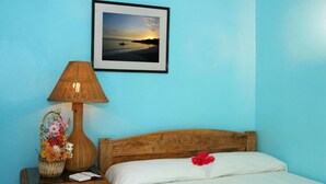 Ein Schlafzimmer mit einem hölzernen Kopfteil, einer Korblampe, einem Blumenkorb und einem gerahmten Bild von einem Sonnenuntergang über dem Wasser.