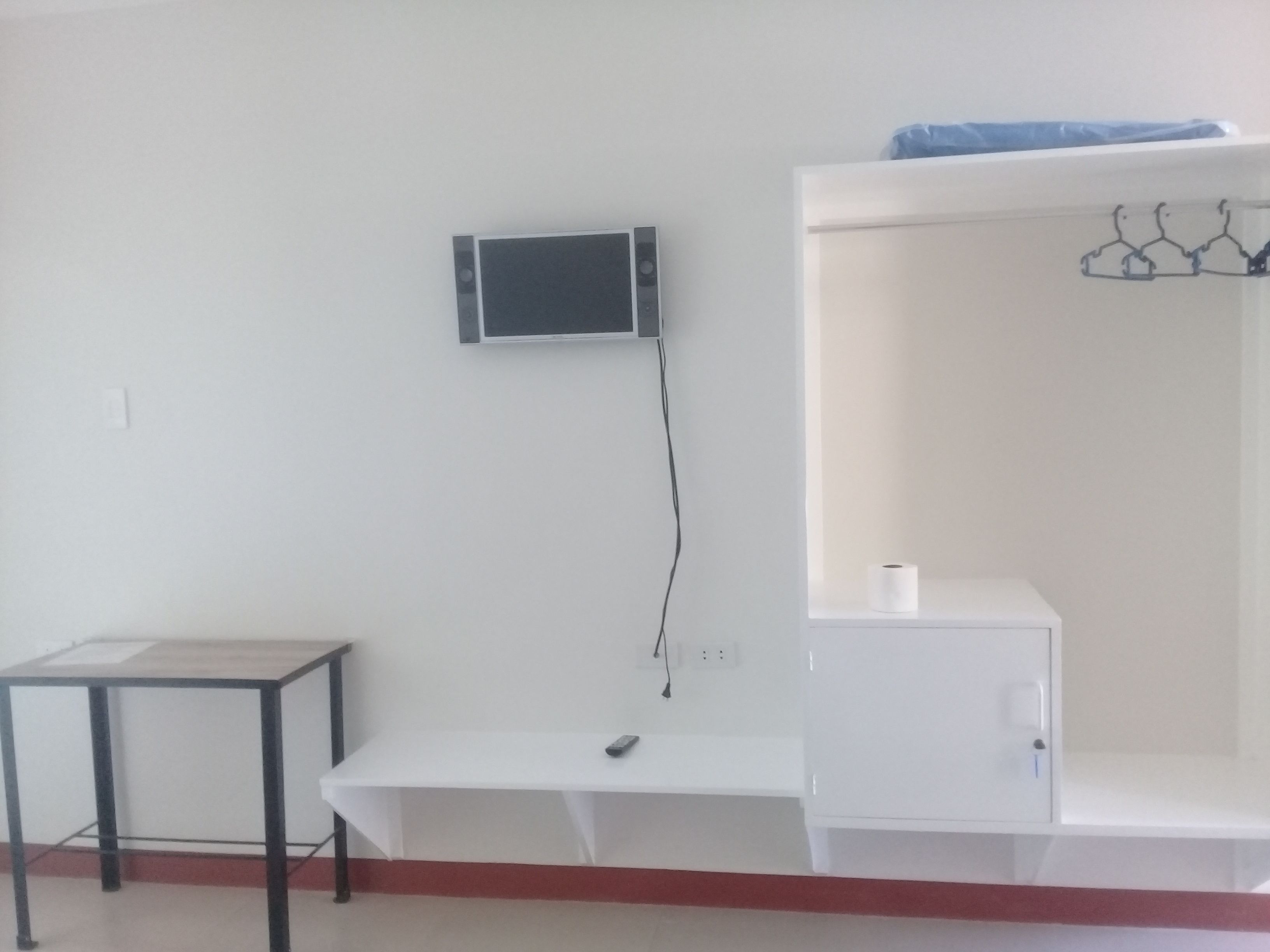 A room with a white desk, a small table, a white cabinet, and a wall-mounted TV.