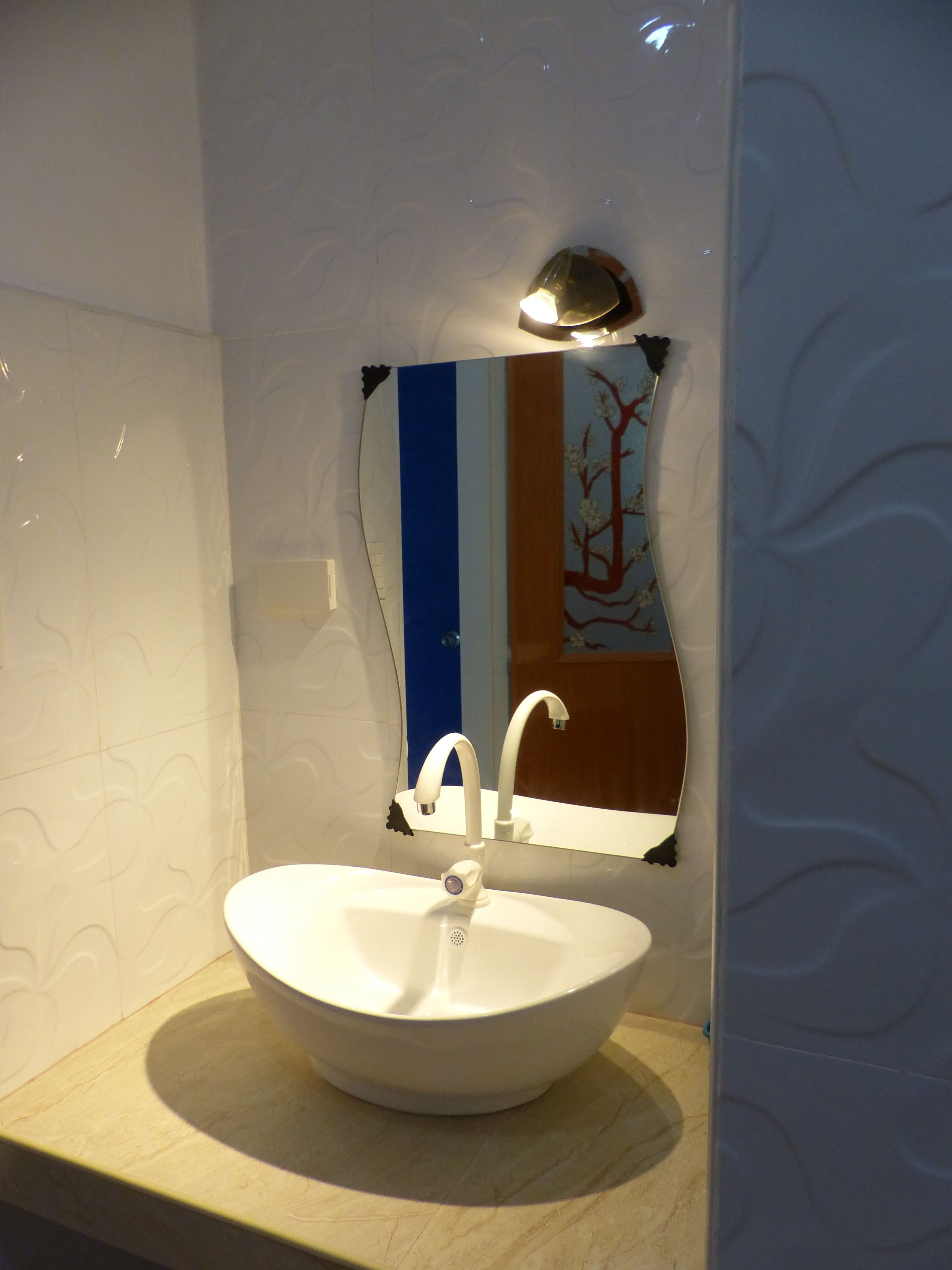 Une salle de bain avec un lavabo blanc, un miroir et un luminaire fixé au mur.