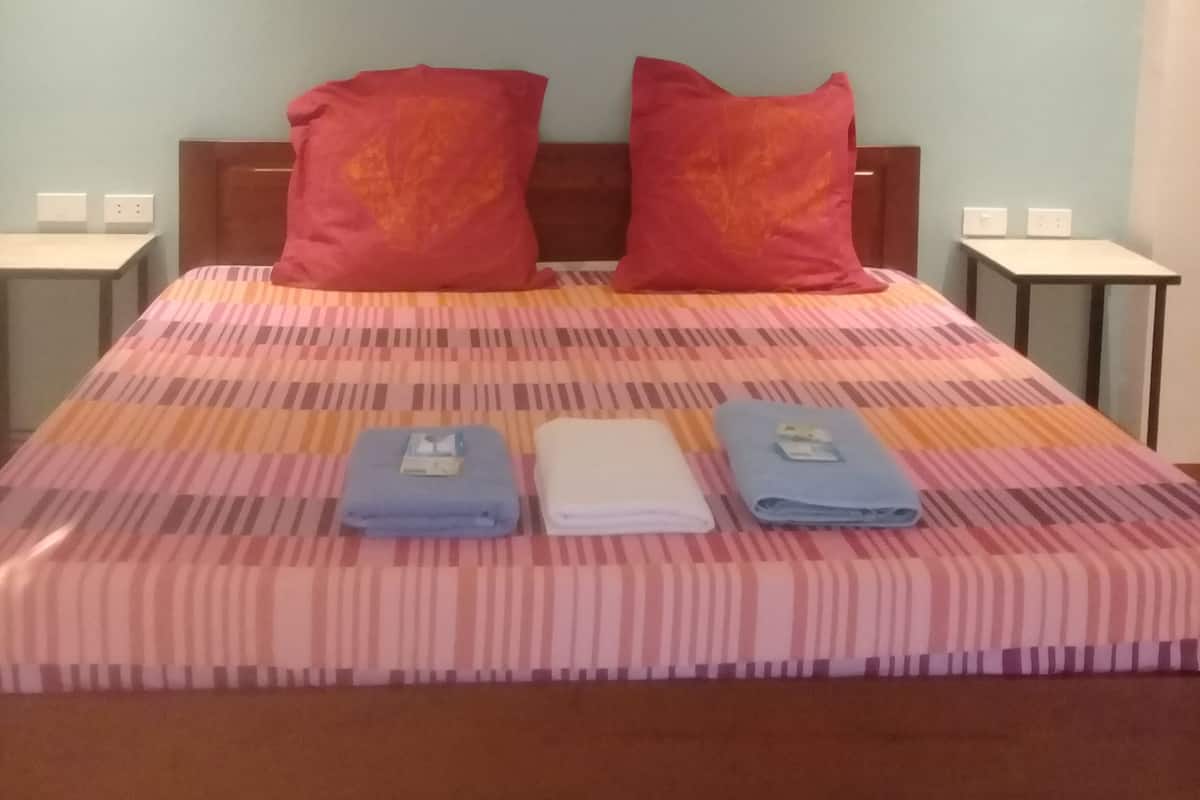 A neatly made bed with a striped bedspread, two pillows, and folded towels on a wooden headboard.