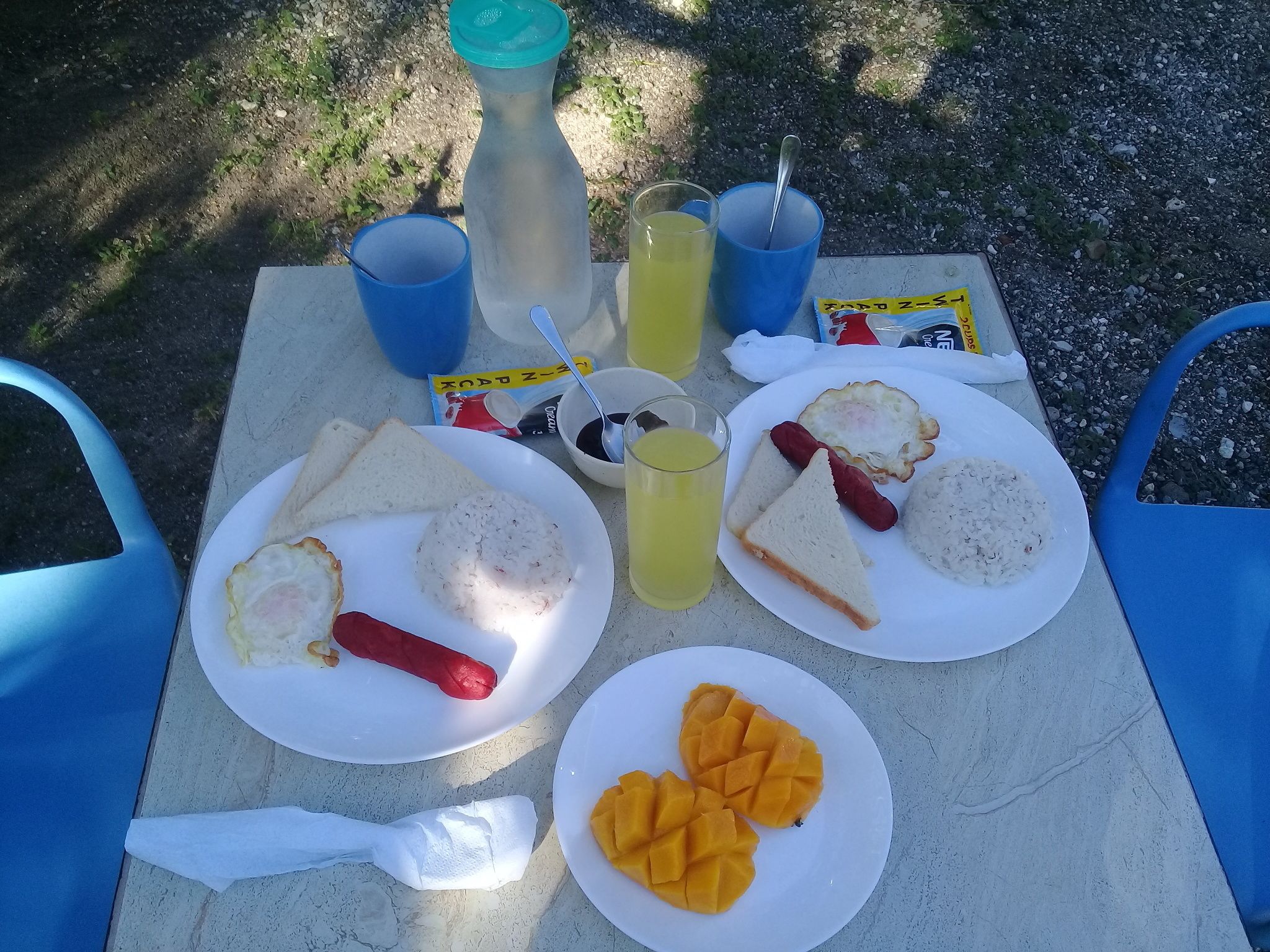 Une table dressée à l’extérieur pour un pique-nique, avec des assiettes remplies de nourriture, des boissons et une bouteille.