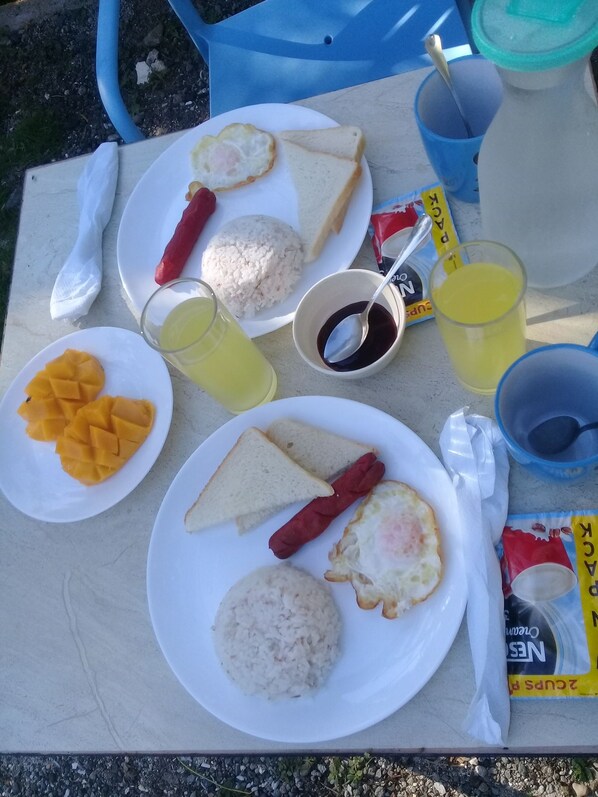 Una mesa con alimentos para el desayuno, como tostadas, huevos, arroz y tajadas de mango.