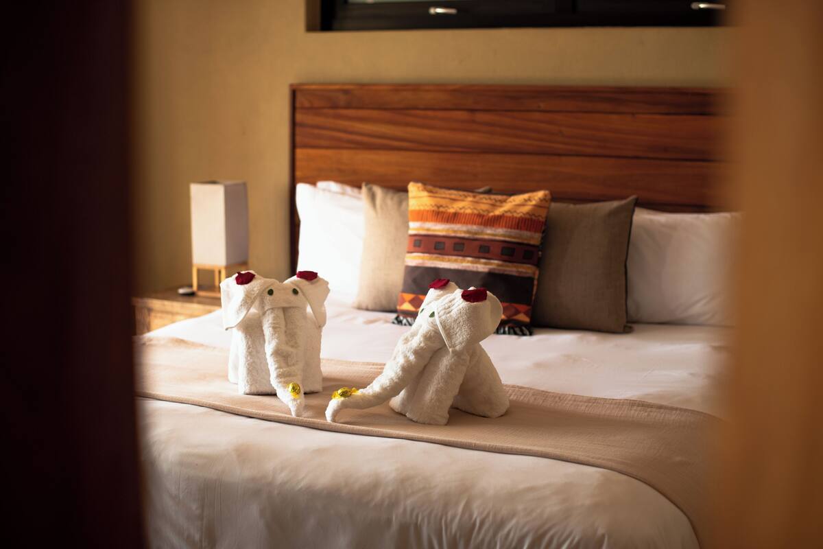 A hotel room with a neatly made bed, a wooden headboard, and two plush elephant-shaped pillows on the bed.