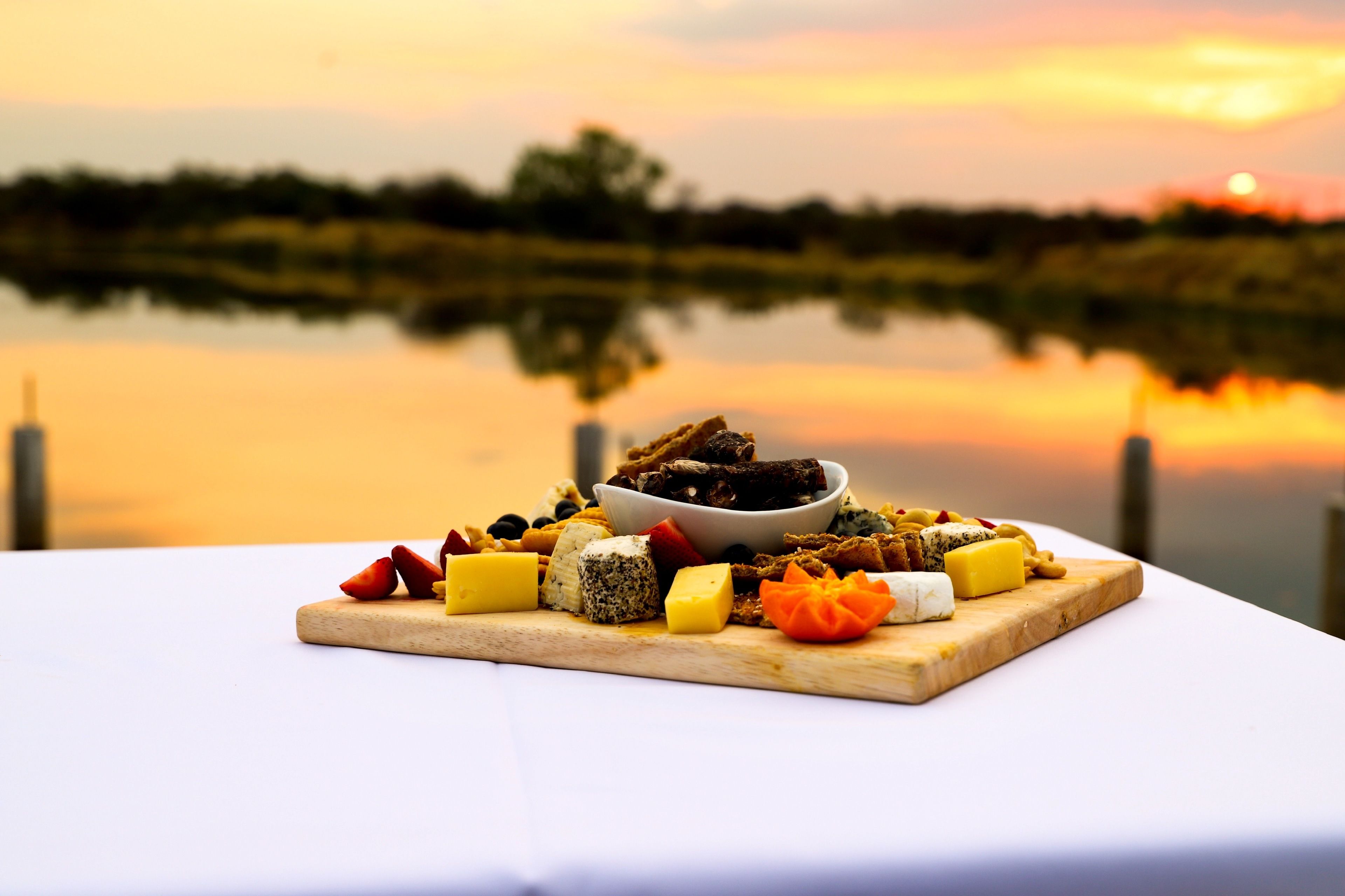 Une assiette de fromages, présentée sur une planche en bois, avec un coucher de soleil en arrière-plan.