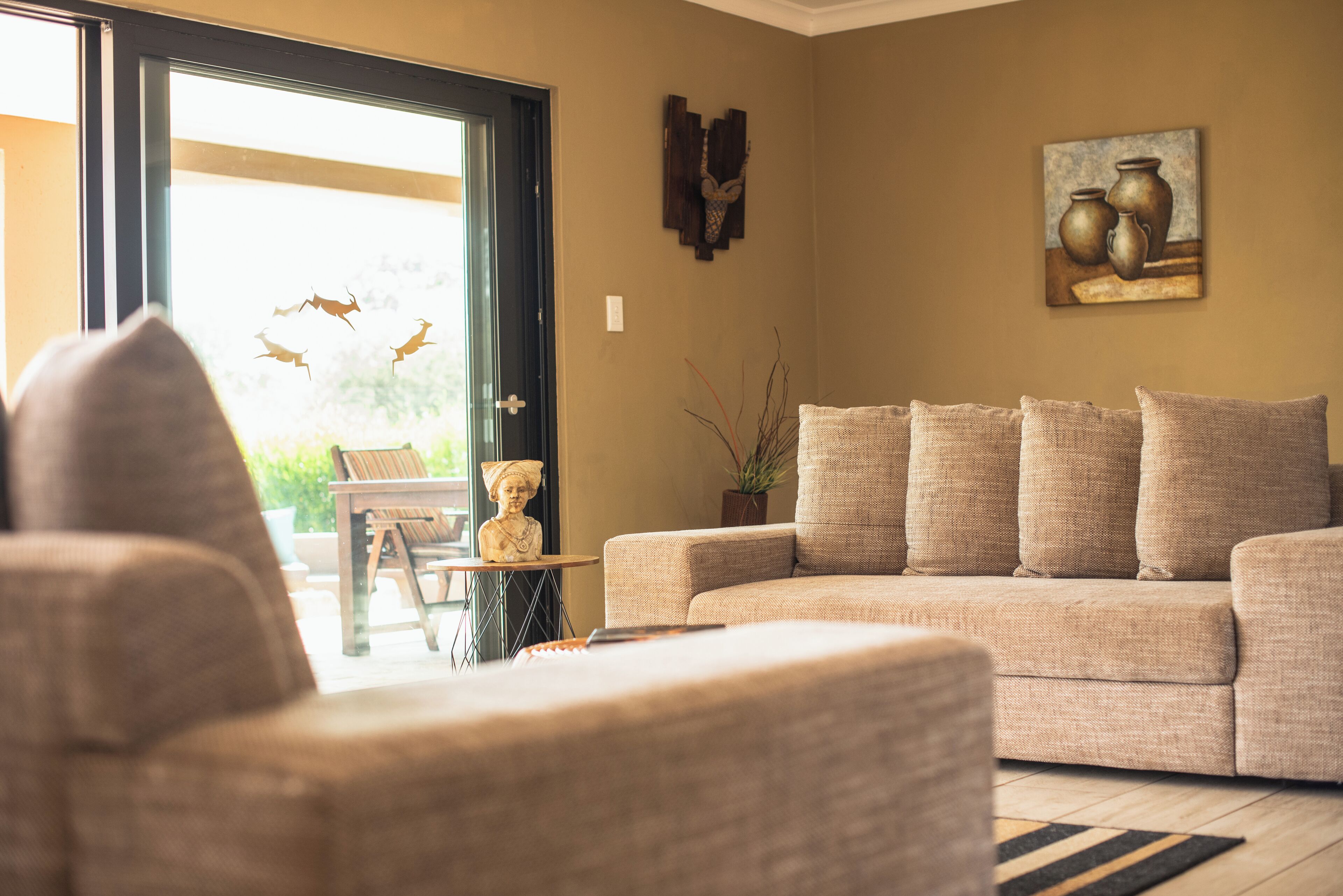 Un salón con un sofá color beige, una pequeña mesa con una estatua y un cuadro en la pared.