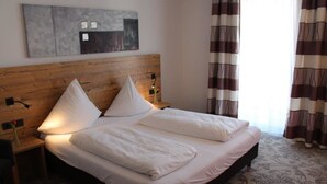 A neatly made bed with white linens and two pillows, a wooden headboard, a bedside table with a lamp, and a wall-mounted artwork. - Hotel Häußler (Reichertshofen)