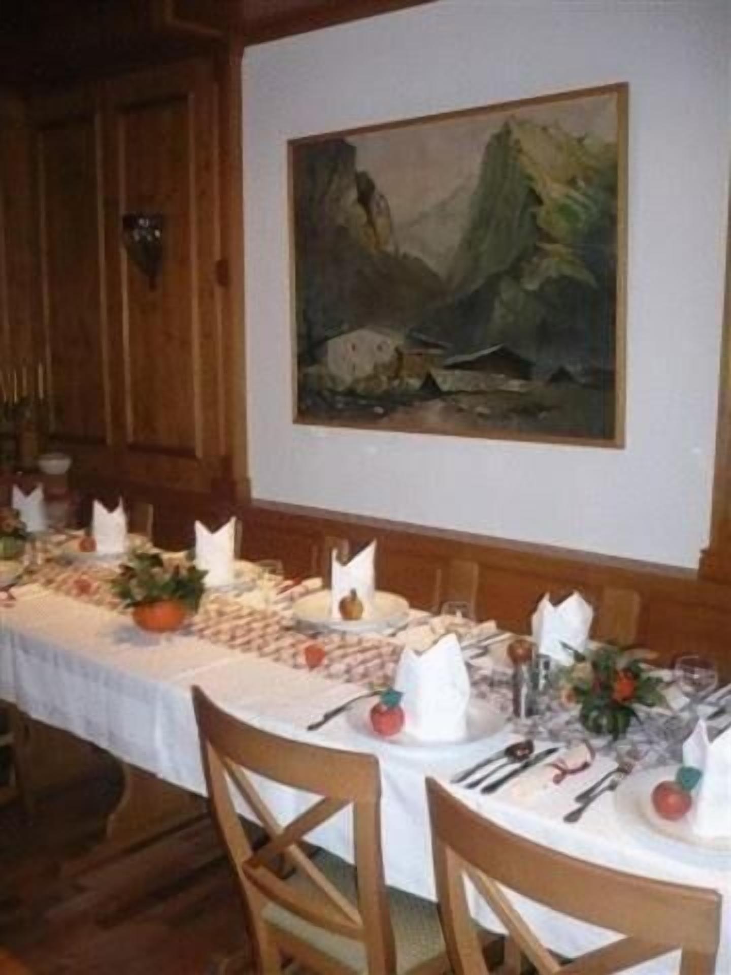 A dining area with a long table set for a meal, wooden chairs, and a painting on the wall.