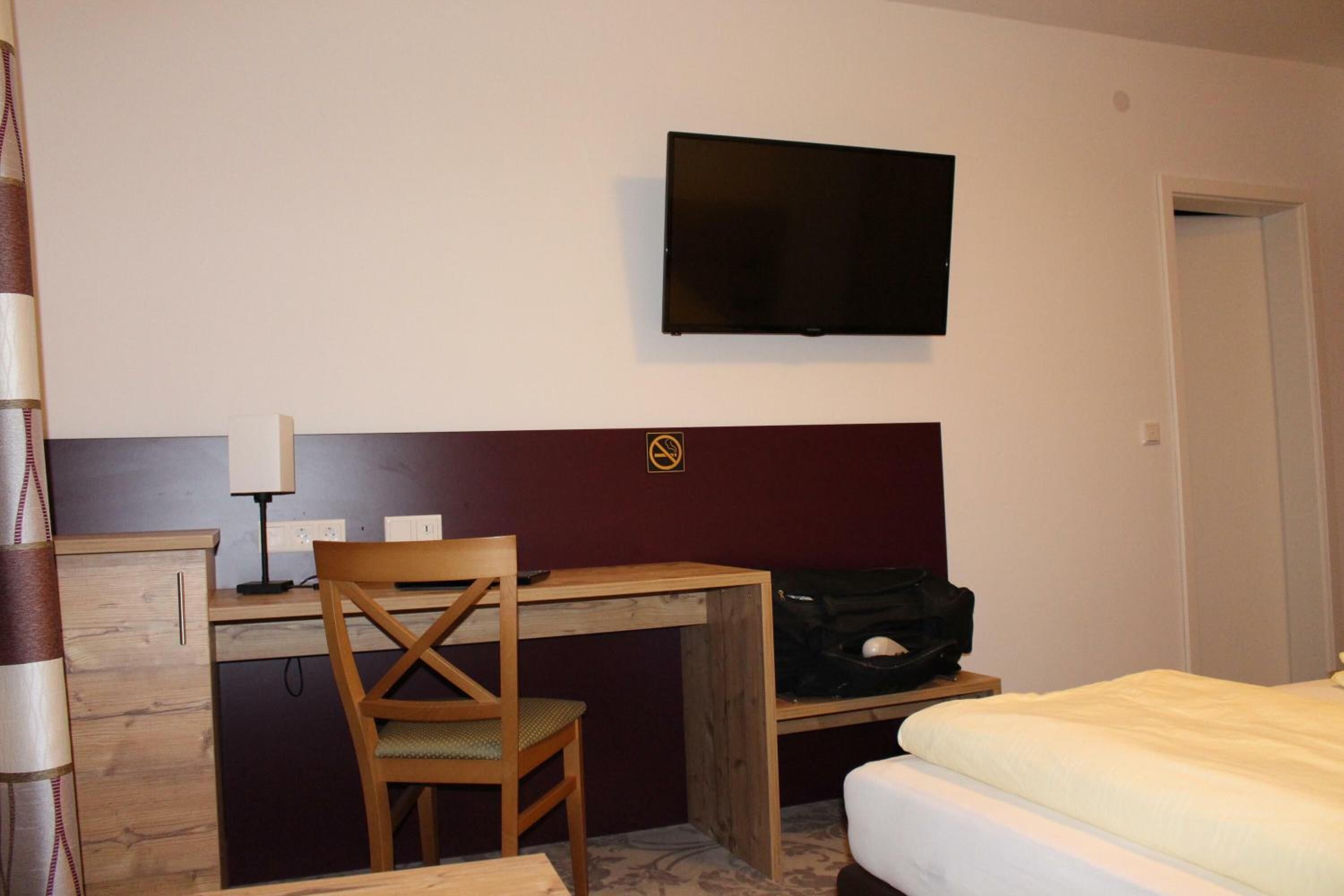 Una habitació d'hotel amb un llit, un escriptori amb cadira, una televisió penjada a la paret i una perxa per a abrics.