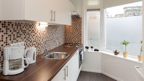 A modern kitchen with a coffee maker, sink, and window with plants. - Bos en Lommer Apartments (Amsterdam)
