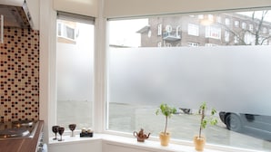 A kitchen with a window overlooking a street, a tiled backsplash, and a small potted plant on the windowsill. - Bos en Lommer Apartments (Amsterdam)